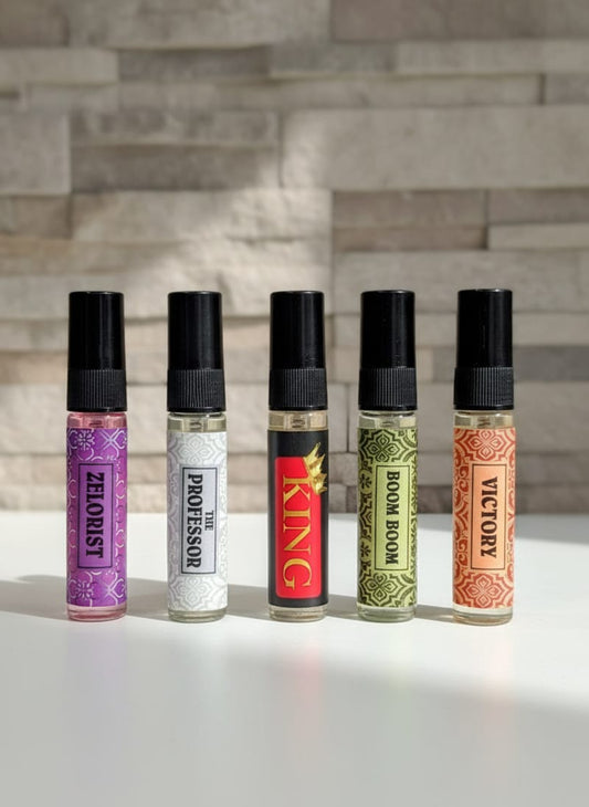 Five small bottles with colorful labels on a reflective surface with a stone wall background